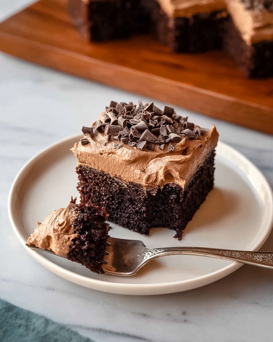 A square piece of chocolate cake sits on a white plate, showing two layers: a dark, moist chocolate base with a thick layer of smooth, light brown chocolate frosting on top. Small dark chocolate curls are sprinkled over the frosting, adding texture and decoration. A silver fork with an ornate handle rests on the plate, holding a small bite of the cake covered in frosting. The plate is placed on a white marbled surface, and a wooden board with more cake pieces is visible in the background. photo taken with an iphone --ar 4:5 --v 7