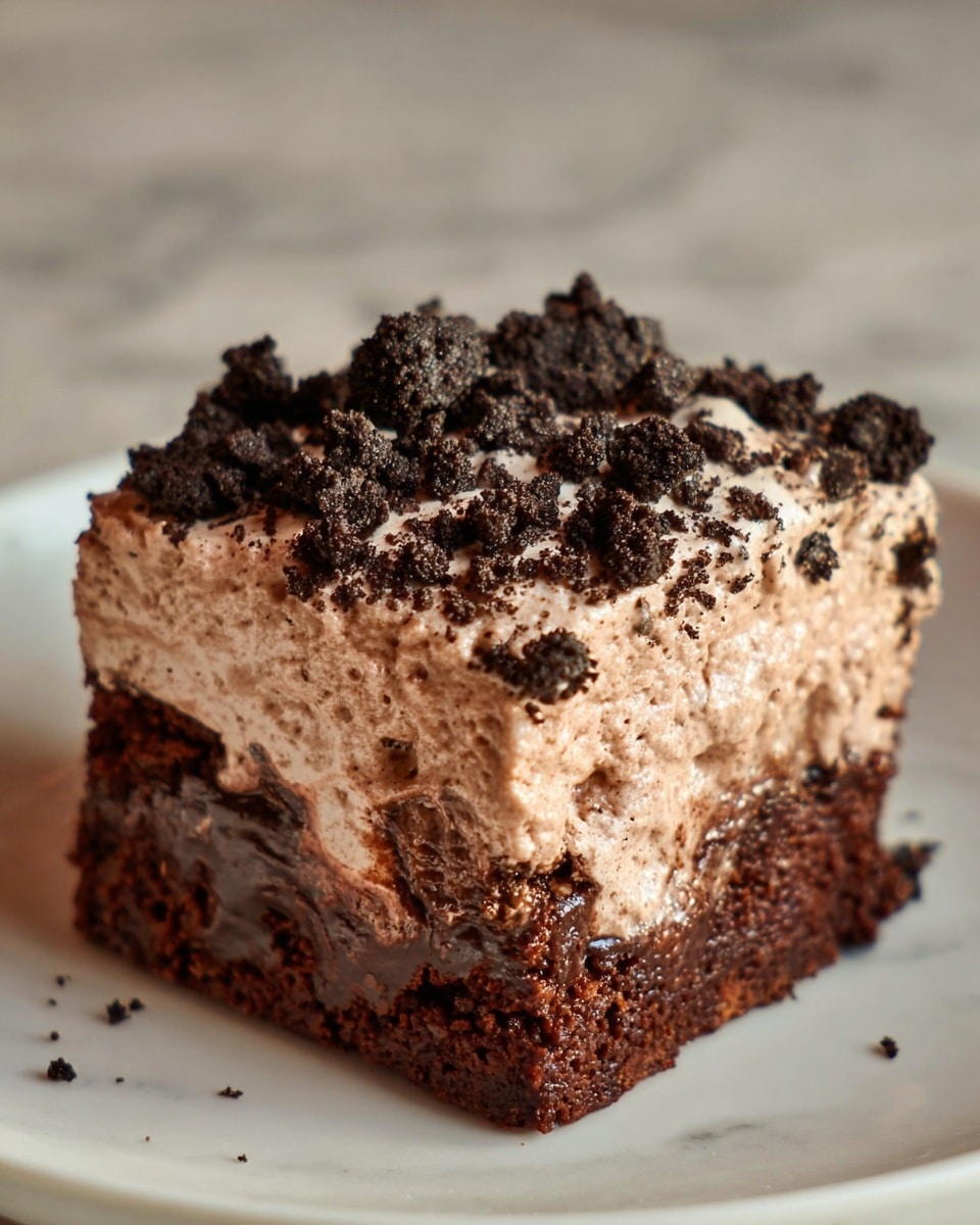 A close-up of a single square piece of chocolate dessert on a white plate with a white marbled texture underneath. The dessert has two main layers: the bottom layer is a rich, dark brown, moist chocolate cake with a slightly gooey texture, showing melted chocolate inside. The top layer is a thick, light brown chocolate mousse with a fluffy, creamy texture, speckled with chunks of dark chocolate cookie crumbs scattered over it. The piece looks soft and indulgent, with some mousse gently spilling over the edges. Photo taken with an iphone --ar 4:5 --v 7