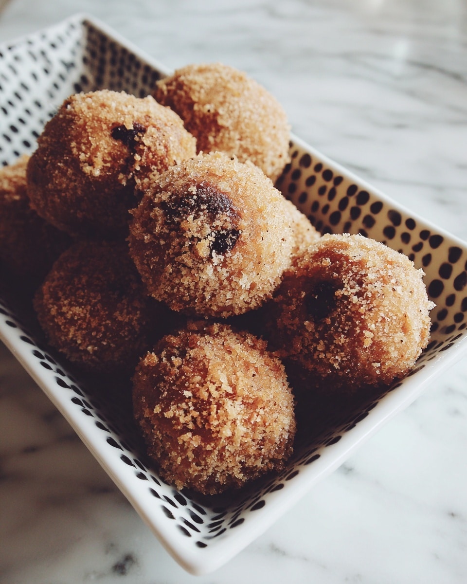 A close-up view of several round balls coated with a crumbly, light brown crumb layer, some showing a darker spot inside, arranged in a pile inside a white rectangular dish with a black and white dotted pattern, sitting on a surface with a white marbled texture. photo taken with an iphone --ar 4:5 --v 7