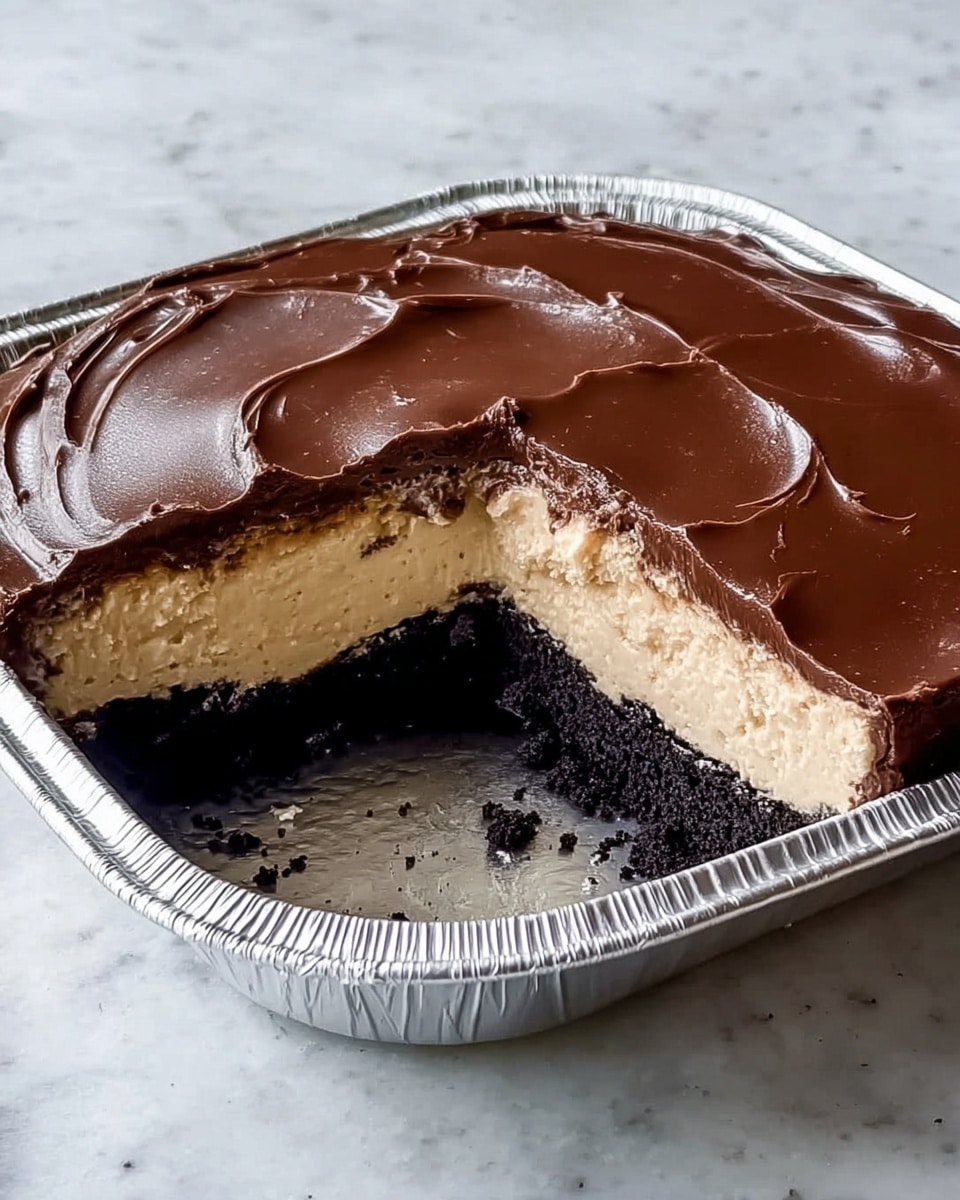 This dessert has three visible layers, placed inside a silver foil pan on a white marbled surface. The bottom layer is dark brown, almost black, with a crumbly texture like a cookie or cake base. The middle layer is thick and creamy with a light beige color, smooth but fluffy in appearance. The top layer is a shiny dark brown chocolate ganache that is smooth with slight ripples, covering the cream evenly. A chunk is missing from the front right corner, showing the inside texture of each layer clearly. photo taken with an iphone --ar 4:5 --v 7