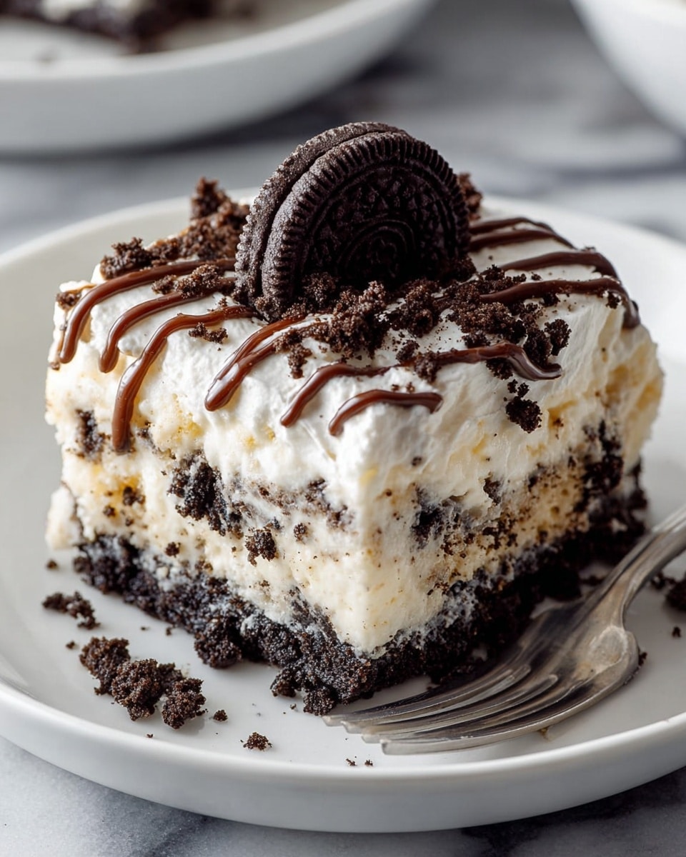 A square piece of cookies and cream dessert sits on a white plate, showing three visible layers. The bottom and middle layers are dark crushed cookie crumbs, and the thick middle layer is creamy white with bits of cookie mixed in. The top layer is fluffy white cream sprinkled with more crushed cookie crumbs, drizzled with thin lines of chocolate sauce, and topped with a whole chocolate sandwich cookie. The plate is set on a white marbled surface with a silver fork resting beside the dessert. Photo taken with an iphone --ar 4:5 --v 7