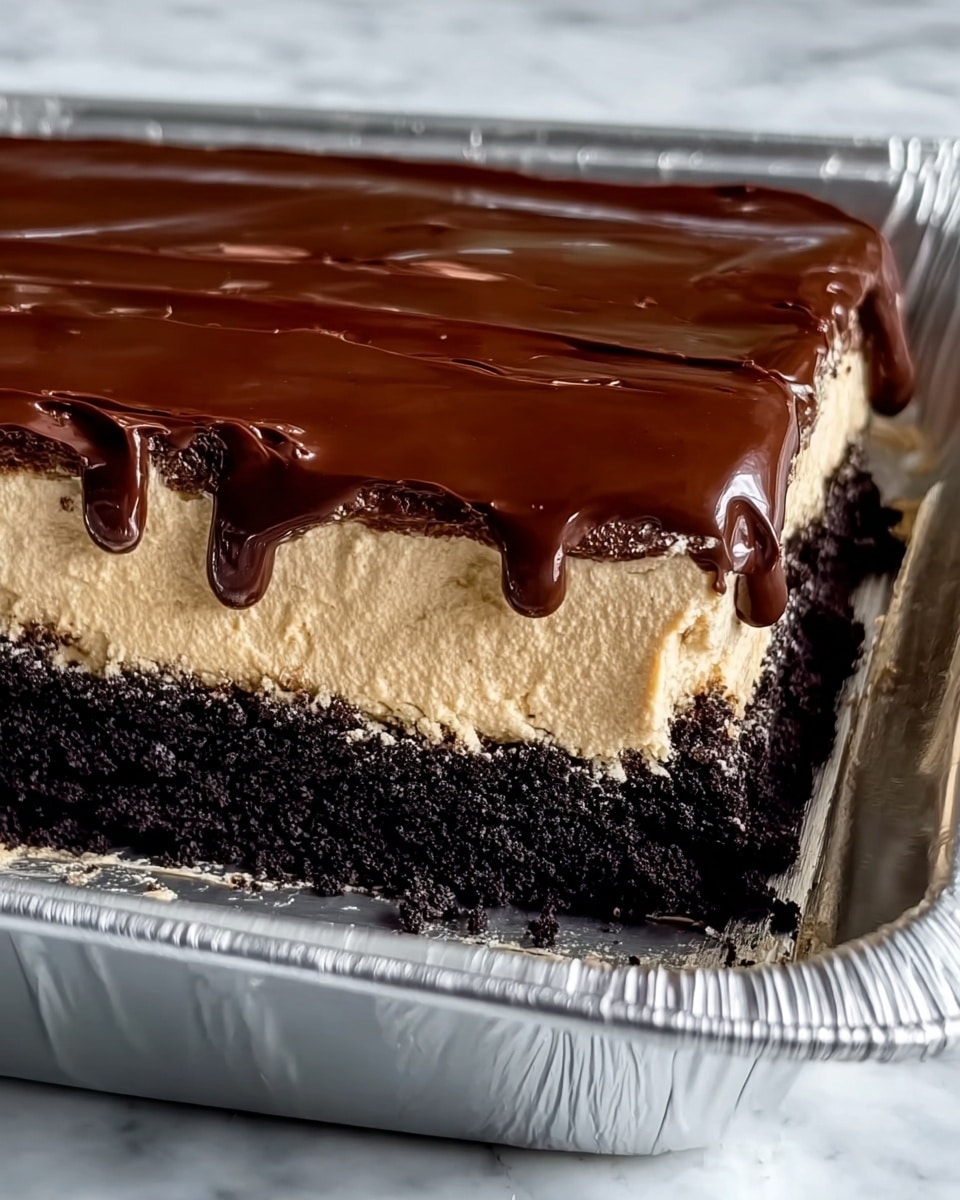 This image shows a three-layered dessert in a rectangular aluminum pan. The bottom layer is a dark, crumbly crust, almost black in color, with a rough texture typical of crushed cookies or cake crumbs. The middle layer is thick and creamy, light beige or coffee-colored, smooth and fluffy like mousse or whipped cream. The top layer is a glossy, rich chocolate ganache, dark brown and shiny, dripping slightly over the edge of the creamy layer, adding a smooth texture contrast. The pan is placed on a white marbled surface. photo taken with an iphone --ar 4:5 --v 7