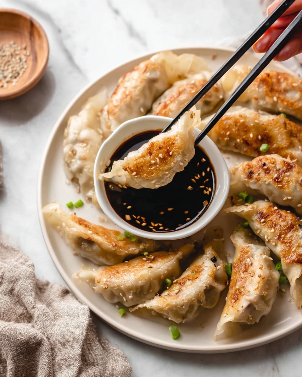 A white plate holds a stack of golden-brown pan-fried dumplings with crispy edges and soft, slightly translucent centers, sprinkled lightly with sesame seeds and small green onion pieces. The dumplings are arranged around a small white bowl filled with dark soy dipping sauce, one dumpling being lifted by black chopsticks held by a woman's hand, partially dipped in the sauce. The plate is on a white marbled surface with a neutral-colored cloth napkin folded nearby. Photo taken with an iphone --ar 4:5 --v 7