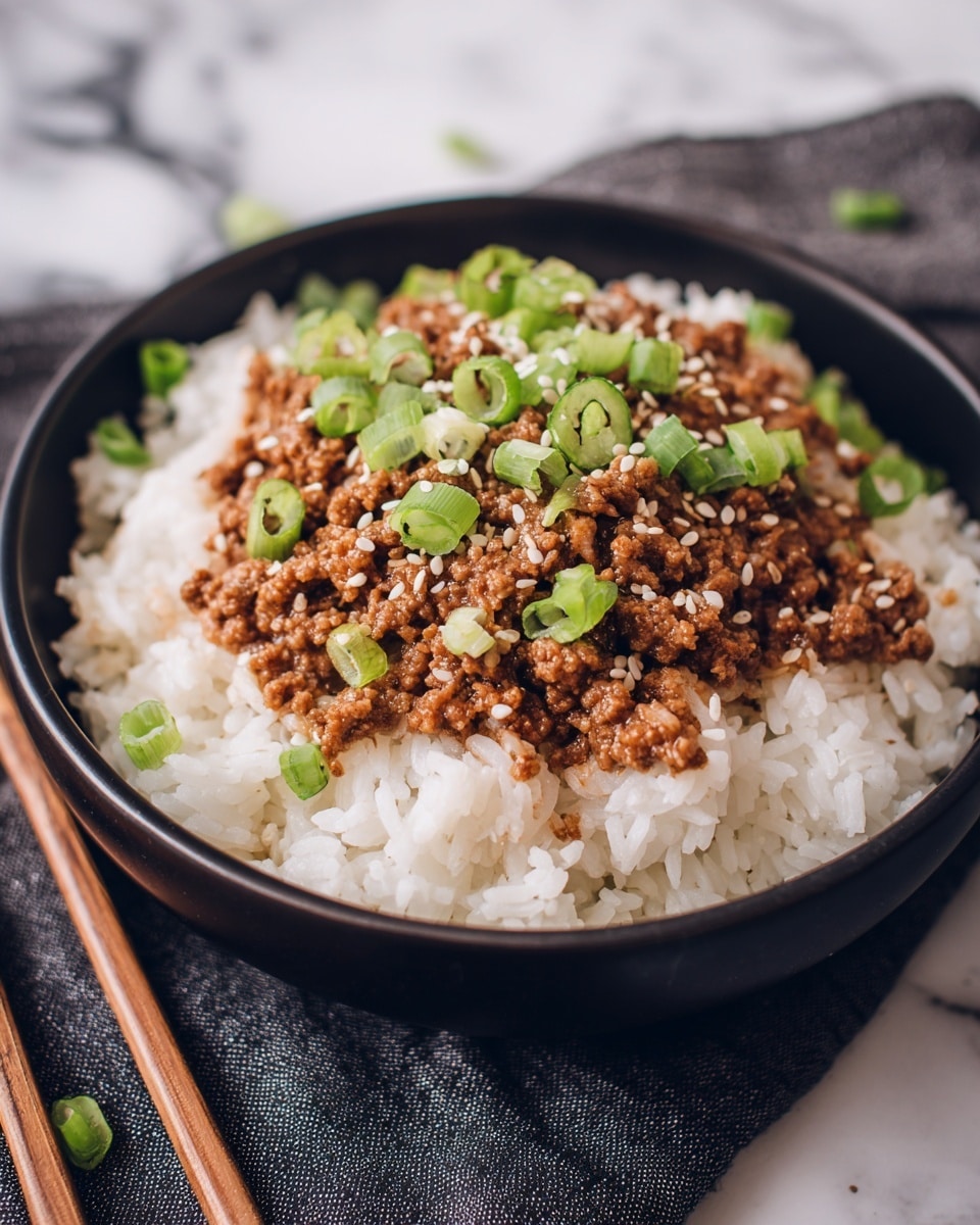 A black bowl contains two main layers: the bottom layer is fluffy white rice with visible grains, and the top layer is cooked minced meat in a brown sauce, covering the rice evenly. On top of the meat, bright chopped green onions are scattered, along with small white sesame seeds, adding texture and color contrast. The bowl sits on a dark cloth over a white marbled surface, with blurred wooden chopsticks placed in the background. photo taken with an iphone --ar 4:5 --v 7