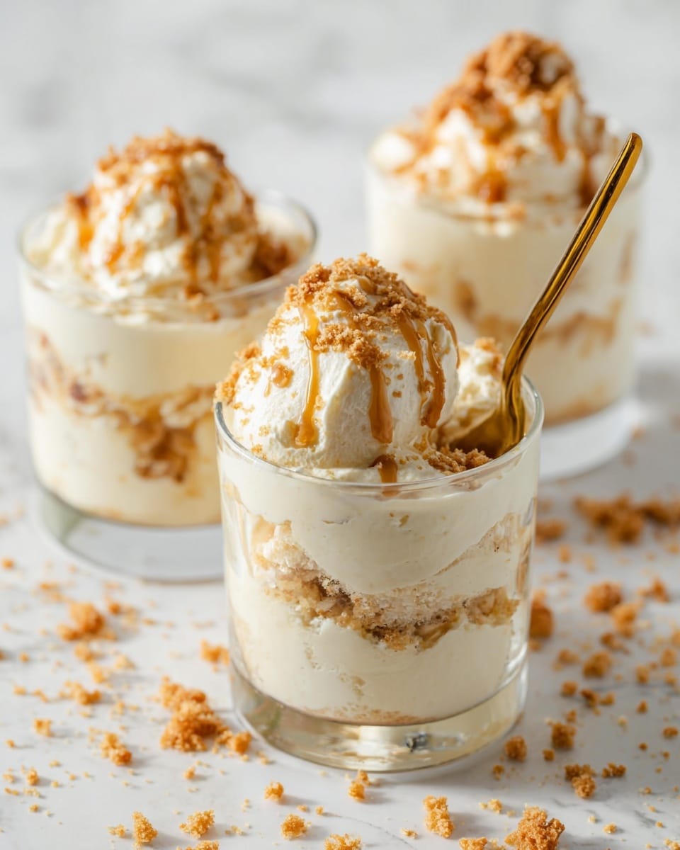 The image shows three clear glass cups filled with a creamy dessert that has several soft, white layers mixed with light brown crumbled bits inside. The bottom layer is smooth and pale, topped by a thick white cream layer with scattered brown crumbs, repeated twice for a total of about four layers. The dessert is finished with a bigger scoop of white cream on top, drizzled with light brown sauce and sprinkled with more crumbs. A golden spoon holds a scoop of the top cream in the front cup. The cups sit on a white marbled textured surface with scattered crumbs around. photo taken with an iphone --ar 4:5 --v 7