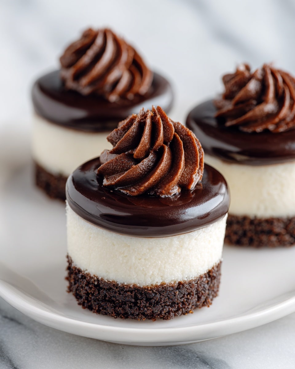 The image shows small round desserts with three distinct layers placed on a white plate. The bottom layer is dark brown and crumbly, resembling a chocolate crust. The middle layer is thick, smooth, and creamy white, contrasting with the dark base. The top layer is a glossy chocolate ganache that covers the creamy layer fully. On top of each dessert, there is a swirl of rich, dark chocolate frosting with a shiny, smooth texture. The background features a white marbled surface, enhancing the dessert's colors. photo taken with an iphone --ar 4:5 --v 7