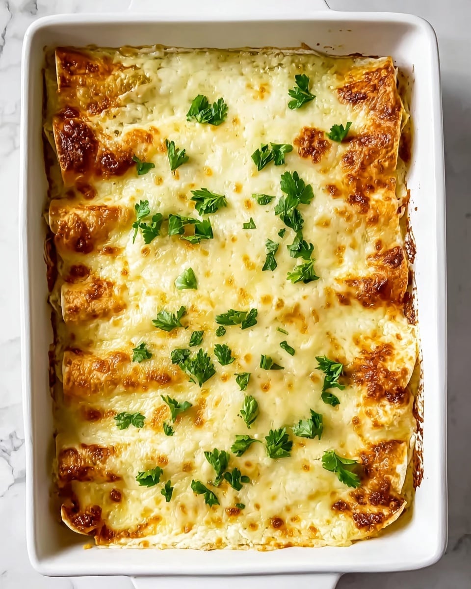 A white square baking dish holds a baked dish with about two layers of rolled tortillas covered evenly in melted, golden-brown cheese. The cheese layer is smooth with small browned spots and bubbly texture along the edges, while fresh green parsley leaves are sprinkled on top for a pop of color. The edges of the tortillas peek out, showing a light golden crispy texture. The dish sits on a white marbled surface. photo taken with an iphone --ar 4:5 --v 7