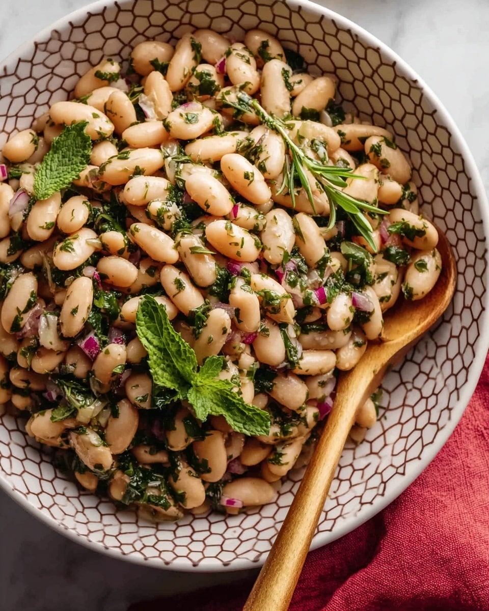 A close-up view of a white bowl with a hexagon pattern filled with a bean salad made of light beige beans mixed with chopped green herbs and small pieces of red onion. The beans look soft and smooth, evenly coated with herbs that add green and dark specks throughout. Fresh herb sprigs and leaves are laid on top, adding a touch of fresh green color. A wooden spoon rests on the side inside the bowl. The bowl is placed on a white marbled textured surface with a hint of a red cloth in the corner. Photo taken with an iphone --ar 4:5 --v 7