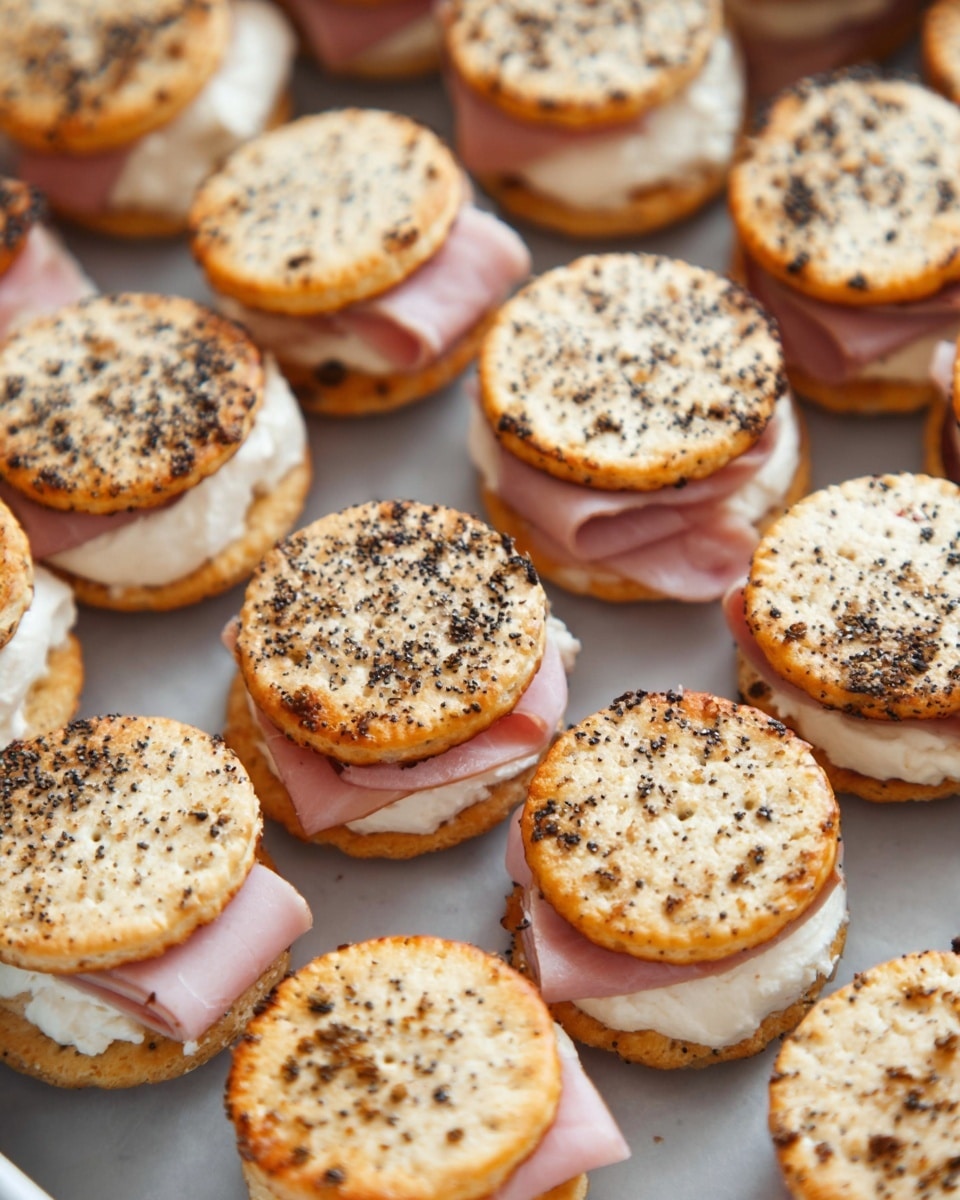 The image shows many small sandwich stacks arranged closely on a flat tray over a white marbled surface. Each sandwich has three visible layers: a round, toasted cracker on top sprinkled with black seeds, a pink slice of ham in the middle, and a thick layer of white cream cheese at the bottom. The crackers are golden brown with some darker toasted spots, and the ham is folded slightly between the crackers and cheese, making the layers clearly separated. The sandwiches are uniform in size and shape, filling the tray evenly. photo taken with an iphone --ar 4:5 --v 7