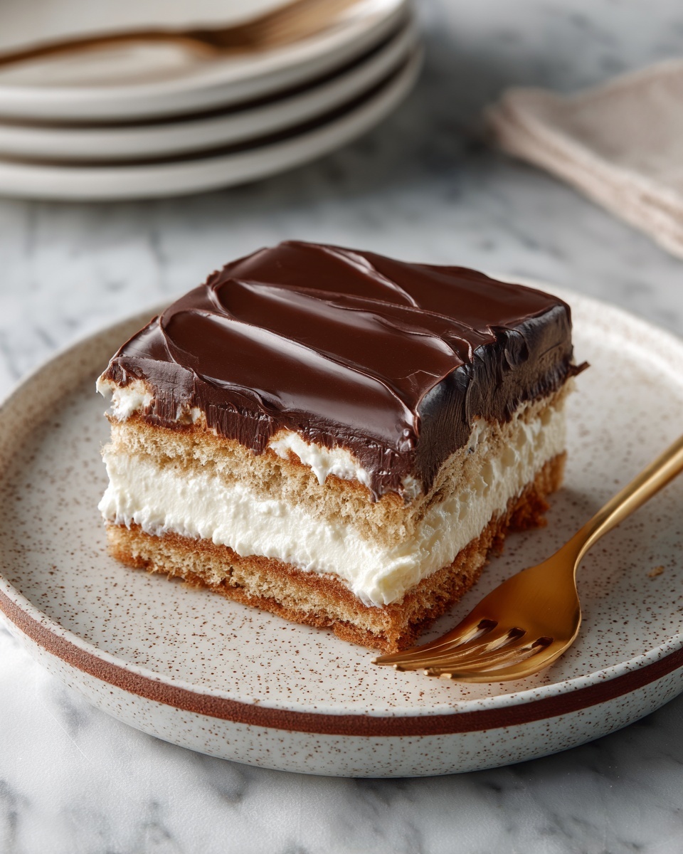 A square dessert with three main layers sits on a white speckled plate with a thin brown rim. The bottom and middle layers are made of light brown biscuit or cake, while two thick creamy white layers separate them. The top of the dessert is covered with a smooth, shiny dark chocolate glaze with gentle waves. A golden fork lies on the plate next to the dessert. The scene is set on a white marbled surface with a soft focus on a stack of white plates in the background. photo taken with an iphone --ar 4:5 --v 7