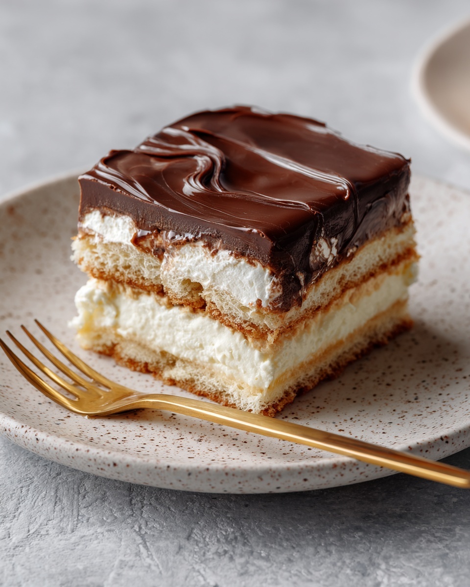 A square piece of layered dessert sits on a white speckled plate, showing three main layers of cream and biscuit. The bottom layer is a light brown biscuit, topped by a thick, fluffy white cream layer, followed by another biscuit layer, then a second thick cream layer. The top is covered with a smooth, glossy dark brown chocolate layer that has gentle swirls on its surface. A golden fork lies on the plate next to the dessert, all placed on a white marbled texture. Photo taken with an iphone --ar 4:5 --v 7