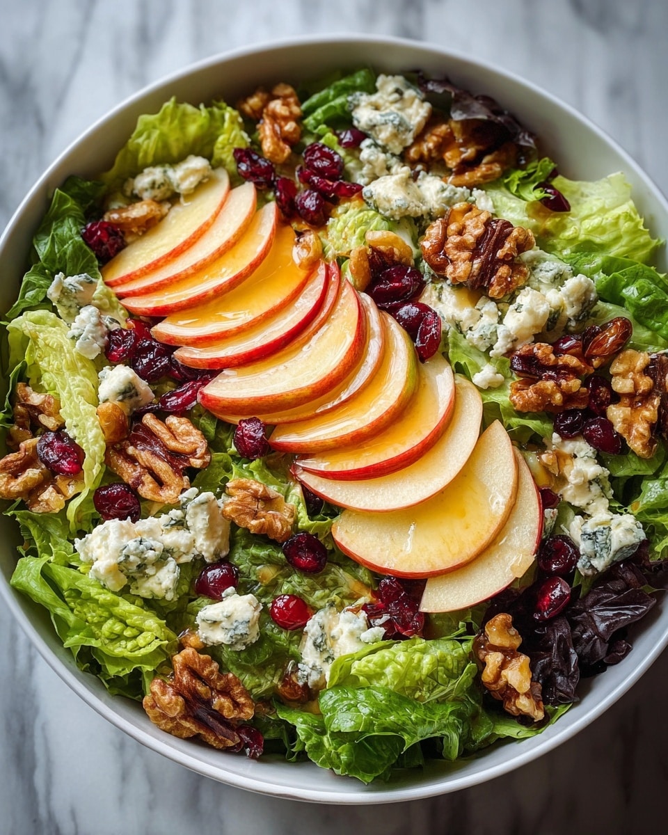 A white bowl holds a fresh mixed green salad as the first layer, with large green leafy lettuce and some darker leaves underneath. The second layer is thin slices of red and yellow apple arranged in three neat fan shapes evenly spaced on top of the greens. Scattered over this are small chunks of white cheese with blue veins, adding a crumbly texture. Next, rich brown walnuts are spread across, adding contrast and crunch, along with bright red dried cranberries scattered around. Everything is lightly coated with a shiny, golden dressing that glistens on the fruits and greens. The bowl sits on a white marbled surface. photo taken with an iphone --ar 4:5 --v 7