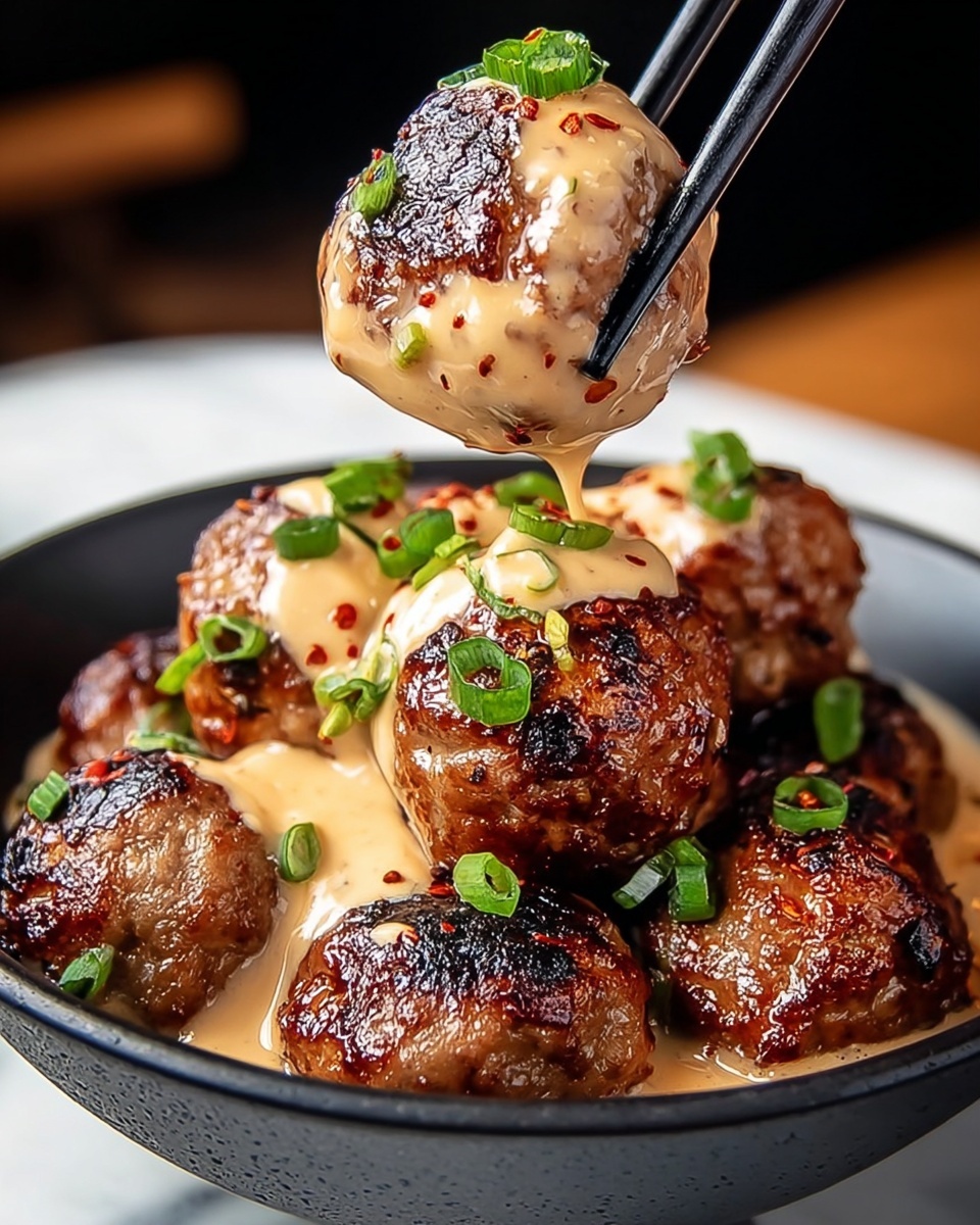 The image shows a close-up of a black bowl filled with about eight grilled meatballs, each covered with a creamy beige sauce speckled with red spices. The meatballs have a shiny, dark brown, slightly charred surface. Some meatballs are topped with small green onion pieces. A pair of black chopsticks is holding one meatball above the bowl, the sauce dripping slightly from it. The bowl sits on a white marbled surface. photo taken with an iphone --ar 4:5 --v 7