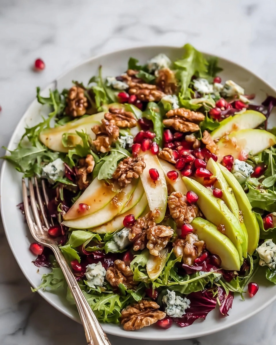 A fresh salad served in a white plate on a white marbled surface. The salad has a base layer of mixed leafy greens with different shades of green and red. On top, there are thin slices of light yellow-green avocado and pear. Scattered over the salad are bright red pomegranate seeds and large pieces of brown walnuts. Small chunks of creamy blue cheese are spread evenly through the salad. The entire dish is lightly drizzled with a glossy dressing. A silver fork rests in the salad, adding depth to the image. photo taken with an iphone --ar 4:5 --v 7