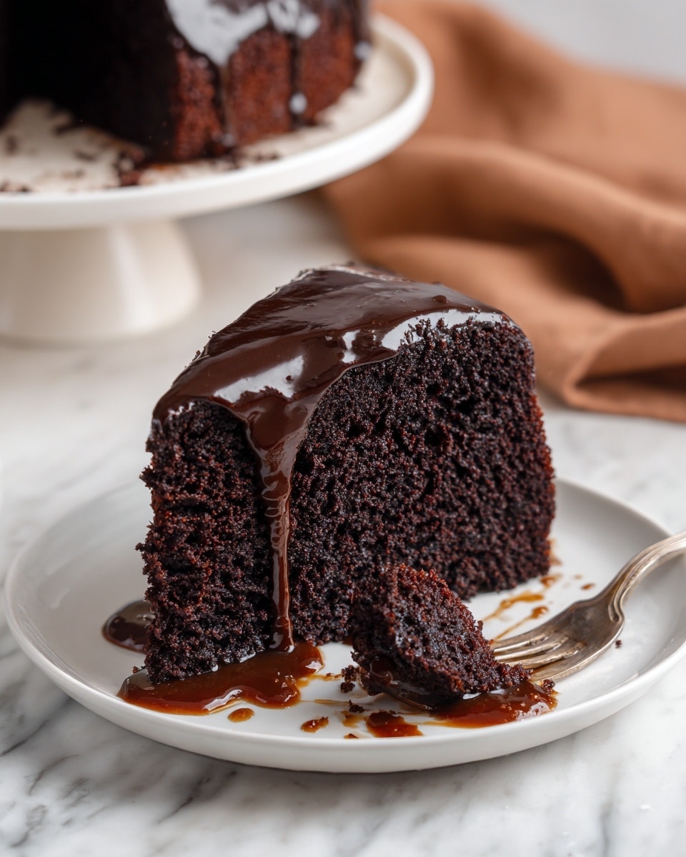 A thick slice of dark moist chocolate cake sits on a white plate with a shiny, smooth dark chocolate glaze dripping heavily over the top and sides. The cake has a dense, crumbly texture with small pockets visible inside. There is a fork resting on the plate with a piece of cake on its tines, and some chocolate sauce is swirled casually on the plate beneath and around the slice. The background includes a soft brown cloth and a blurred white cake stand showing more cake in the distance, all on a white marbled surface. photo taken with an iphone --ar 4:5 --v 7