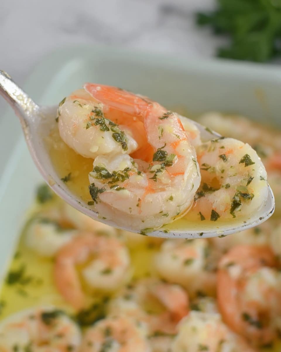 A close-up of soft, cooked shrimp with a pink and white color, sitting in a light yellow buttery sauce with green herbs scattered on top. The shrimp are plump and shiny, resting in a white ceramic spoon held above a dish filled with more shrimp and sauce. The background is a soft white marble texture, with hints of green parsley nearby. The image highlights the shrimp's texture and the rich sauce around them, with a calm and clean look. photo taken with an iphone --ar 4:5 --v 7