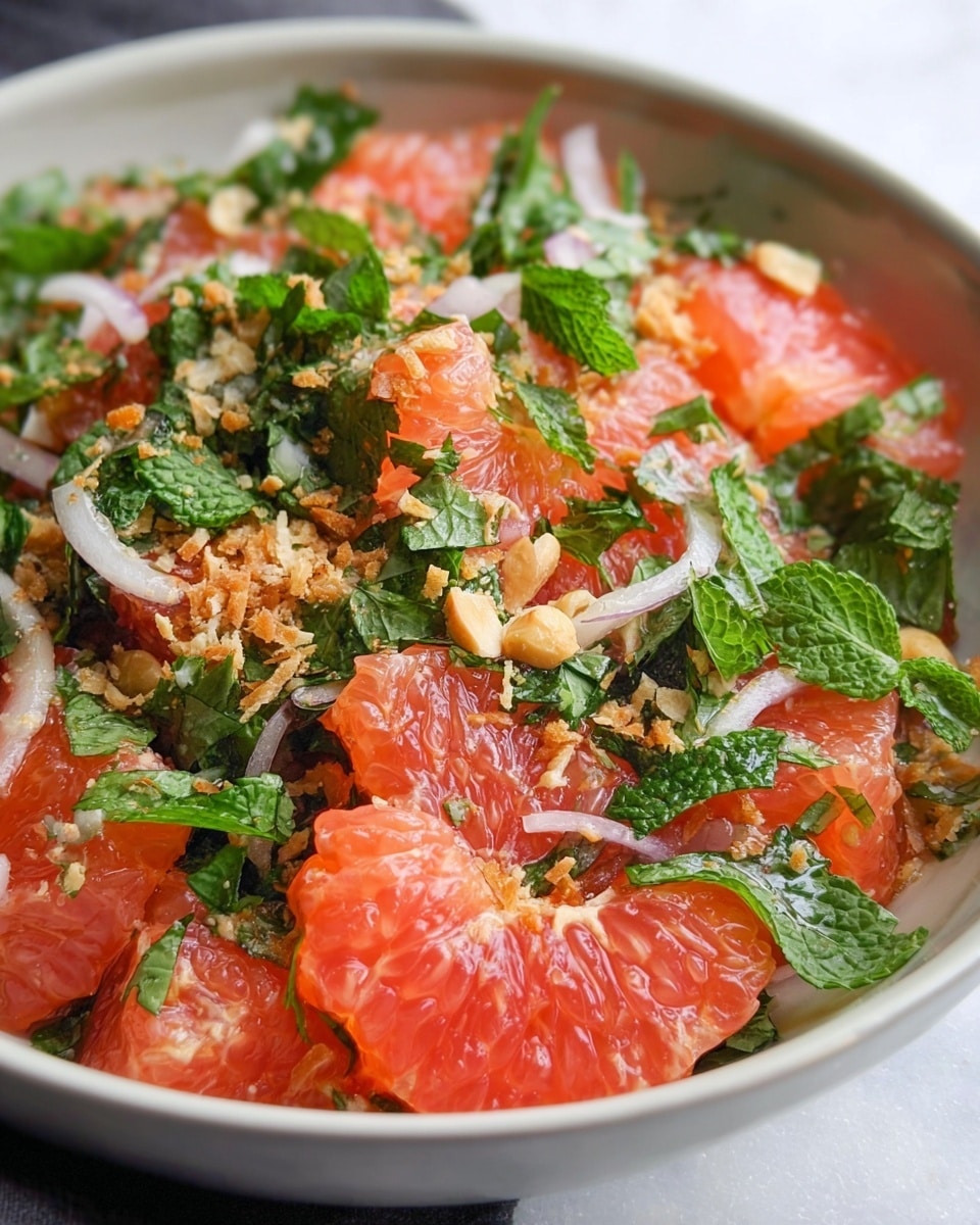 A close-up view of a mixed salad in a white bowl, filled with bright pink grapefruit chunks as the main layer, showing juicy and translucent segments. Mixed throughout are fresh green mint leaves and cilantro, adding a leafy texture, along with thin slices of light purple onions scattered on top. Small crushed peanuts and finely grated light brown toasted coconut sprinkle over the fruit and herbs, adding a crunchy and textured finish. The white marbled surface under the bowl adds a clean, bright background. Photo taken with an iphone --ar 4:5 --v 7