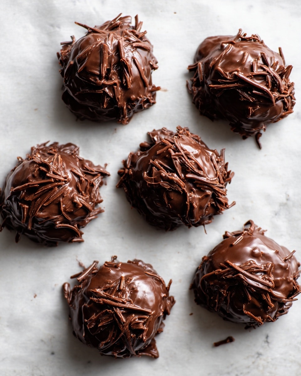 Six uneven mounds of a sticky, glossy chocolate mixture sit spaced out on a flat sheet of parchment paper. Each mound is textured with visible small sticks or shredded pieces of something light brown, tangled into the thick chocolate coating, creating a rough surface of mixed smooth shiny chocolate and rough fibrous bits. The background is subtle white marbled texture. photo taken with an iphone --ar 4:5 --v 7