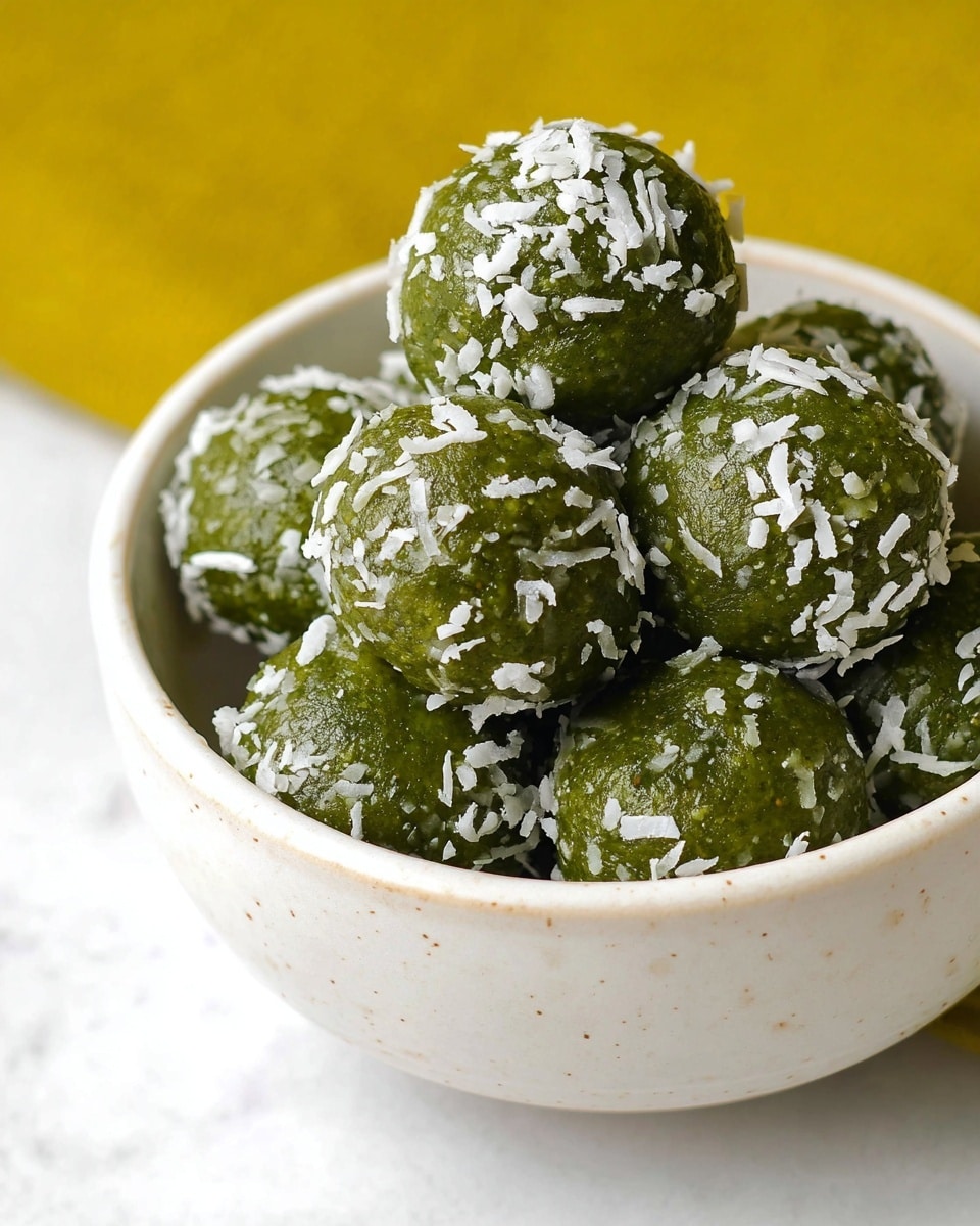 A white bowl filled with several round green balls covered with white shredded coconut pieces, creating a rough texture on their surface. The green balls are packed closely, showing their smooth yet slightly uneven texture. The bowl rests on a white marbled surface, and the background behind the bowl is a soft yellow color. The lighting highlights the shiny, moist look of the green balls, making the white coconut flakes stand out clearly. photo taken with an iphone --ar 4:5 --v 7