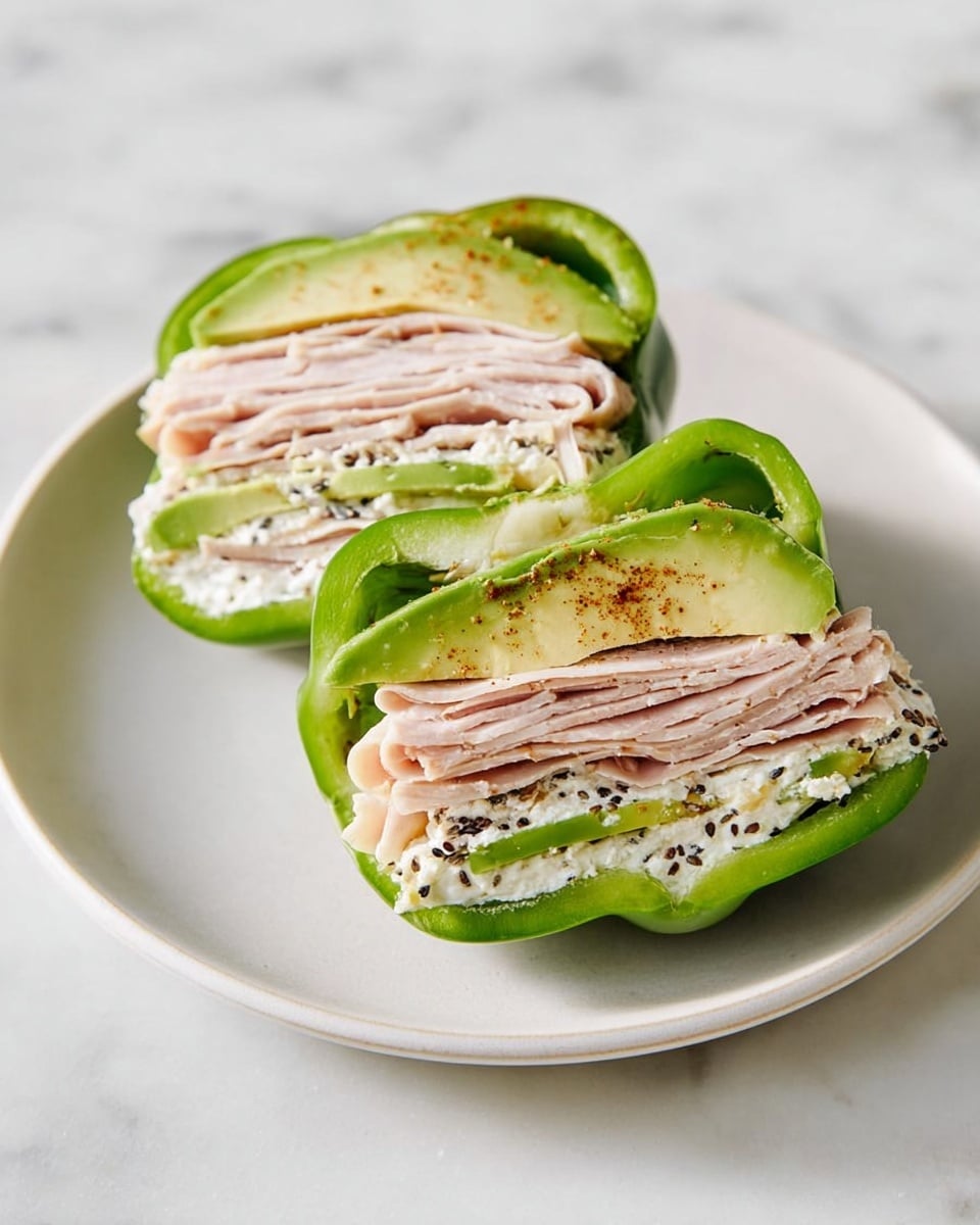 The image shows a white plate with two halves of a green bell pepper stuffed with layers of food. Inside each pepper half, there are multiple thin layers of light pink turkey slices folded neatly. Between the turkey slices, there are slices of light green avocado. Around the turkey and avocado layers, there is a spread of white creamy cheese mixed with small black and brown seeds, adding texture to the filling. The green pepper acts as a thick outer shell holding the stacked layers inside. The plate sits on a white marbled surface. photo taken with an iphone --ar 4:5 --v 7